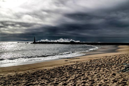 Giant waves breaking on the breakwater and the lighthouse on Aguda Beach, Miramar, Arcozelos town