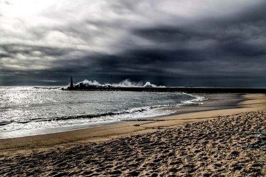 Giant waves breaking on the breakwater and the lighthouse on Aguda Beach, Miramar, Arcozelos town