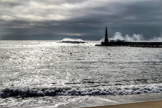 Giant waves breaking on the breakwater and the lighthouse on Aguda Beach, Miramar, Arcozelos town