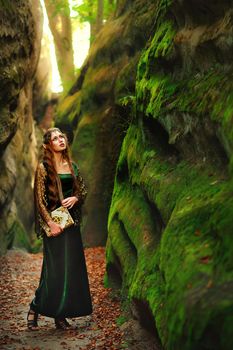 Vertical full length shot of a beautiful long haired young female elf in a dress walking in the forest looking around holding an old book copyspace mystery fairytale myth legendary creature cosplay.