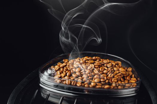 fresh roasted coffee beans with smoke in coffeemaker bean container, close-up view