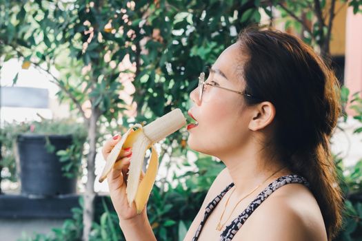 Asian woman in glasses with a red nail polish and a lip stick eating a ripe banana