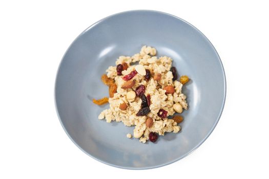 Top view close up of oatmeal with dried fruits and raisins in blue plate on white background. Concept of breakfast with appetizing porridge to support the figure.