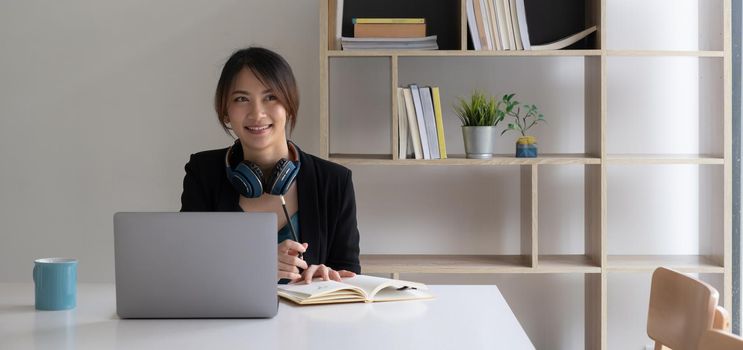 Portrait of a student sitting at her desk at home, studying online with a laptop and writing notes in a notebook