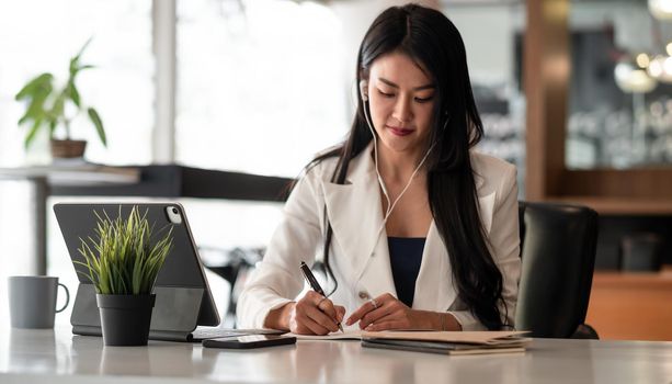 Businesswoman with earbuds for video conference lecture note.woman using tablet webinar video course at home office.