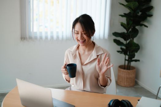 A joyful woman with cup of coffee concentrates on a webinar on her laptop computer