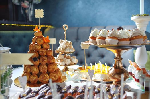 dressing table with sweets, candy pyramid decorated with orange butterflies, cupcakes on a tray, festive table with desserts.