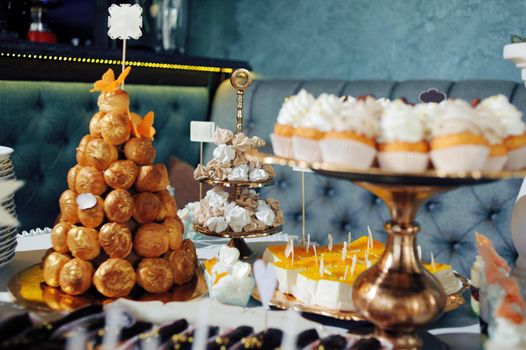 dressing table with sweets, candy pyramid decorated with orange butterflies, cupcakes on a tray, festive table with desserts.
