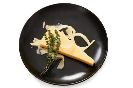 Top view of modern elegant black plate with juicy appetizing piece of cheese with sprig of rosemary on white background. Concept of delicious food with good composition. 
