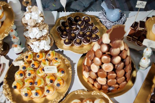 dressing table with sweets, candy pyramid decorated with orange butterflies, cupcakes on a tray, festive table with desserts.