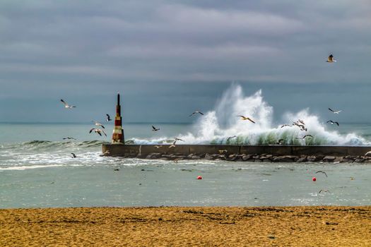 Giant waves breaking on the breakwater and the lighthouse on Aguda Beach, Miramar, Arcozelos town