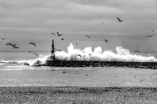 Giant waves breaking on the breakwater and the lighthouse on Aguda Beach, Miramar, Arcozelos town