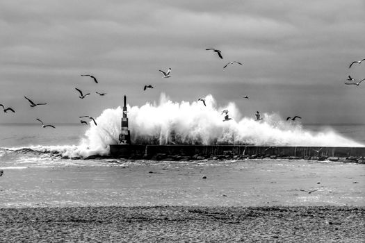 Giant waves breaking on the breakwater and the lighthouse on Aguda Beach, Miramar, Arcozelos town