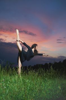 beautiful, flexible, athletic, curly dancer performs vertical side splits in grassy field at sunrise.