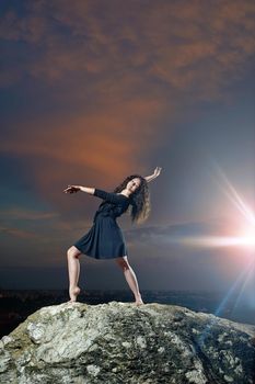 pretty, young, smiling dancer posing while standing on a rock at sunset.