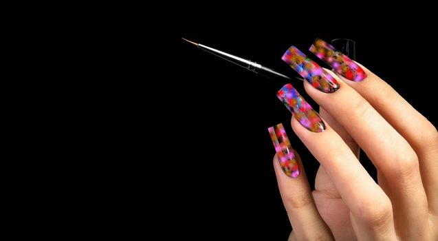 Hand with a beautiful manicure and a brush on a black background. Nail design. Extended nails.
