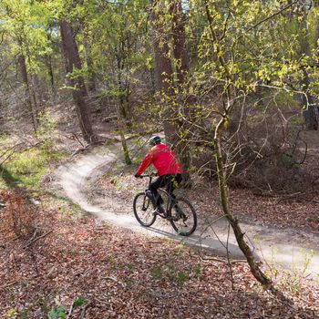 man in red rides mountain bike in spring forest near utrecht in the netherlands