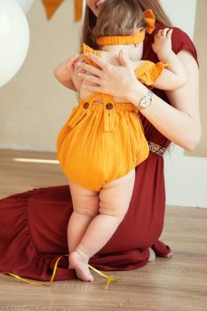 A child in yellow clothes stands with his back to the camera leaning on his mother.