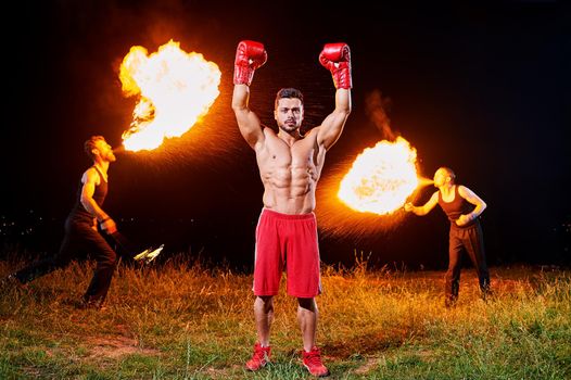 Victorious boxing champion celebrating winning his fight with his arms up in the air extreme fire show with fire eaters on the background copyspace fighting championship achievement happiness winner.