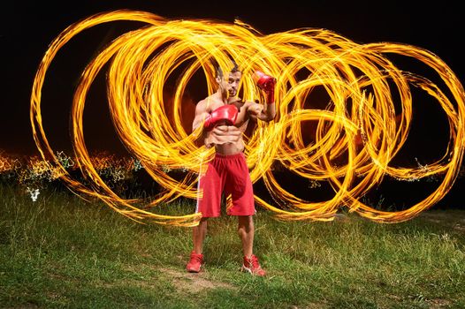 Shot of a young shirtless male fighter with strong fit and toned muscular body training outdoors at night fire and flames on the background copyspace burning fiery flame hot masculinity courage fight.