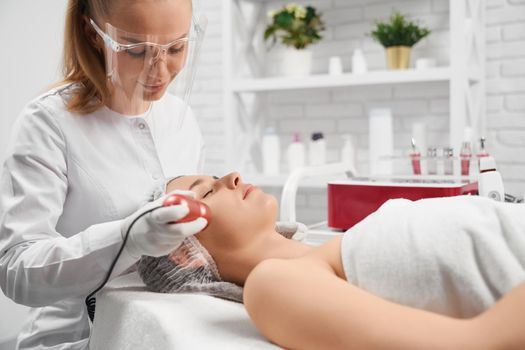 Side view of woman lying on sofa on procedure cleaning face in professional salon. Concept of special beauty procedure for improvements skin face and body. 