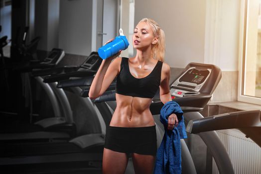 Horizontal shot of a beautiful young fitness woman in workout clothing sweating after training drinking water standing next to a treadmill copyspace gym studio sportswoman drink vitality lifestyle.