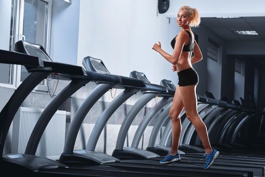 Horizontal full length shot of a happy young fitness woman smiling to the camera while working out at the gym running on a treadmill copyspace lifestyle healthcare body abs muscles strength energetic.