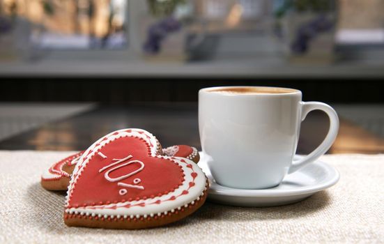 Cup of coziness. Closeup shot of red glazed Valentine s day cookies near a cup of delicious cappuccino
