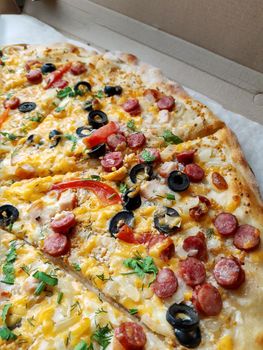 Sliced large pizza lies on the table close-up.