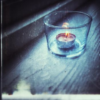 Retro photo of candle in glass. Blue tones with yellow flame.