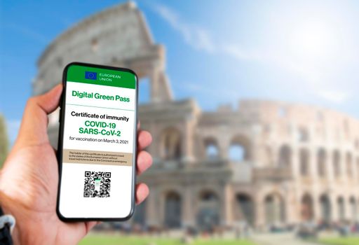 The digital green pass of the european union with the QR code on the screen of a mobile held by a hand with blurred colosseum in the background. Immunity from Covid-19. Travel without restrictions.