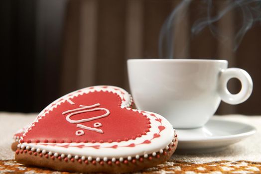 Full of joy. Cup of warm coffee steaming next to a gingerbread glazed cookie