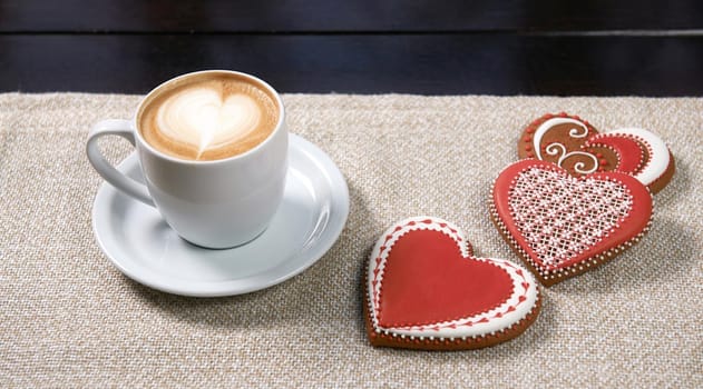 Cup of warmth. Closeup shot of a cup of coffee with red heart shaped cookies on the table