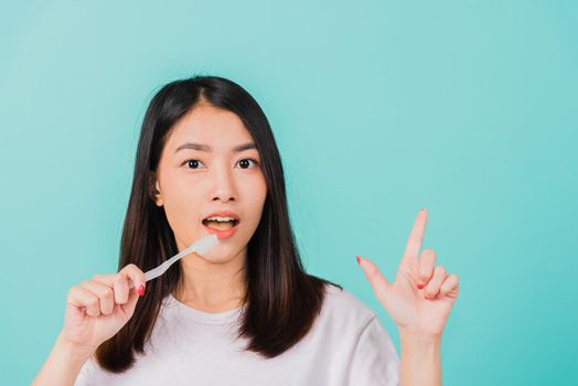 Portrait Asian beautiful young woman teen smiling holding toothbrush brushing teeth in the morning pointing finger to empty space studio shot isolated on blue background, Dental health concept