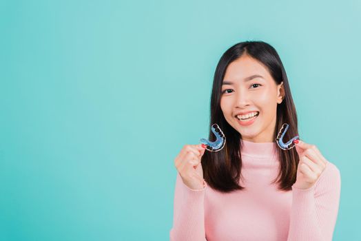 Portrait Asian beautiful young woman smiling hold silicone orthodontic retainers for teeth, Teeth retaining tools after removable braces, isolated blue background, Dental hygiene healthy care concept