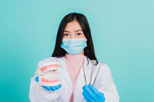 Asian beautiful woman dentist holding professional tool and model teeth denture, female doctor checking denture studio shot isolated on blue background. Dental hygiene surgery health care concept