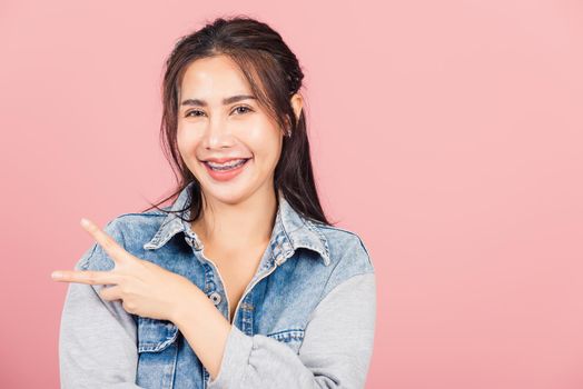 Asian happy portrait beautiful cute young woman wear denim smile stand show finger making v-sign victory sign gesture side away look to camera studio shot isolated on pink background with copy space