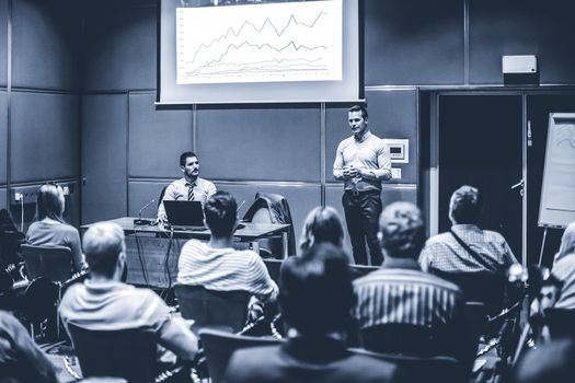 Speaker giving a talk in conference hall at business event. Unrecognizable people in audience at conference hall. Business and Entrepreneurship concept. Blue toned black and white.