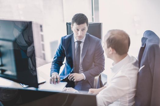 Image of two corporate businessmen discussing a bisiness problem at meeting in modern trading office. Businesspeople sitting at the boardroom and discussing business-plan.