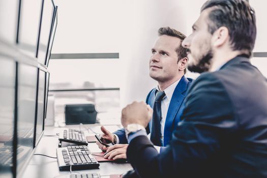 Successful businessmen trading stocks. Stock traders looking at graphs, indexes and numbers on multiple computer screens. Colleagues in traders office. Business success. Successful businessmen trading stocks. Stock traders looking at graphs, indexes and numbers on multiple computer screens. Colleagues in traders office. Business success.