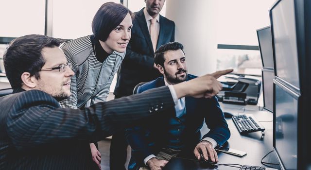 Business team looking at data on multiple computer screens in corporate office. Businessman pointing on screen. Business people trading online. Business, entrepreneurship and team work concept.