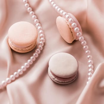 Girly, bakery and branding concept - Sweet macaroons and pearls jewellery on silk background, parisian chic jewelry, French dessert food and cake macaron for luxury confectionery brand, holiday gift