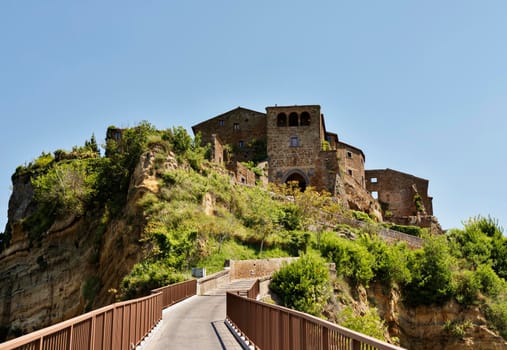 View of Civita di Bagnoregio , old town in central Italy founded by Etruscans , it's known as La città che muore -the dying town -, in the foreground a footbridge