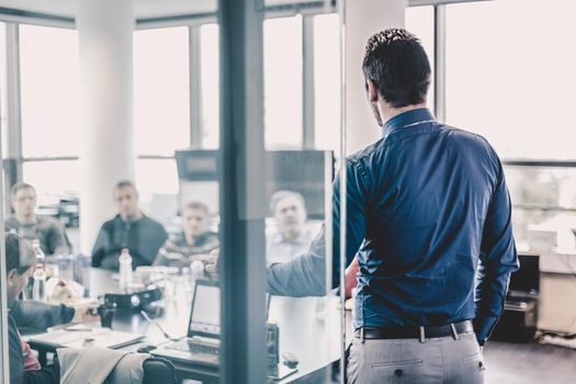 Businessman making a presentation at office. Business executive delivering a presentation to his colleagues during meeting or in-house business training. Rear view. Business and entrepreneurship.