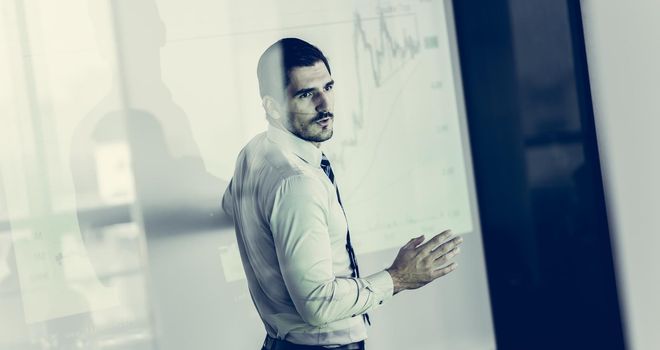 Business man making a presentation in front of whiteboard. Business executive delivering a presentation to his colleagues during meeting or in-house business training. View through glass.