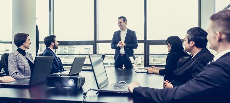 Successful team leader and business owner leading informal in-house business meeting. Businessman working on laptop in foreground. Business and entrepreneurship concept.