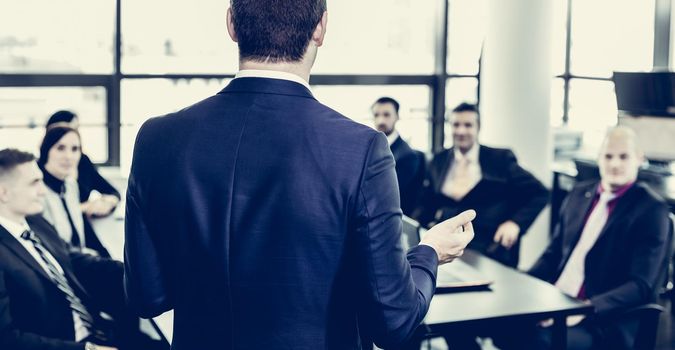 Successful team leader and business owner leading informal in-house business meeting. Businessman working on laptop in foreground. Business and entrepreneurship concept.