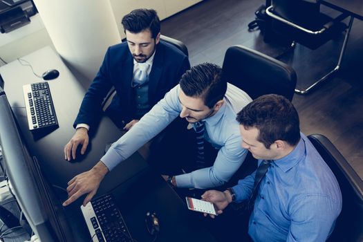 Businessmen trading stocks. Stock traders looking at graphs, indexes and numbers on multiple computer screens. Colleagues in discussion in traders office. Business success concept.