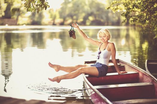 Carefree young blonde woman enjoying the sunny summer day on a vintage wooden boats on a lake in pure natural environment on the countryside.