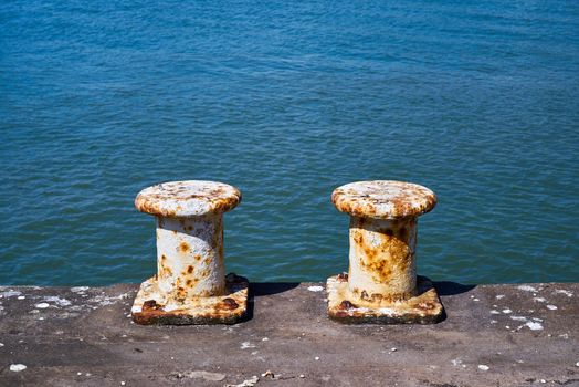 Each white painted steel mooring bollard is showing signs of rust. The pillar bollards are used by ships to moor while in dock.